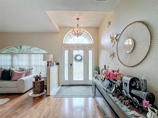 foyer entrance featuring a wealth of natural light, wood-type flooring, a textured ceiling, and a notable chandelier