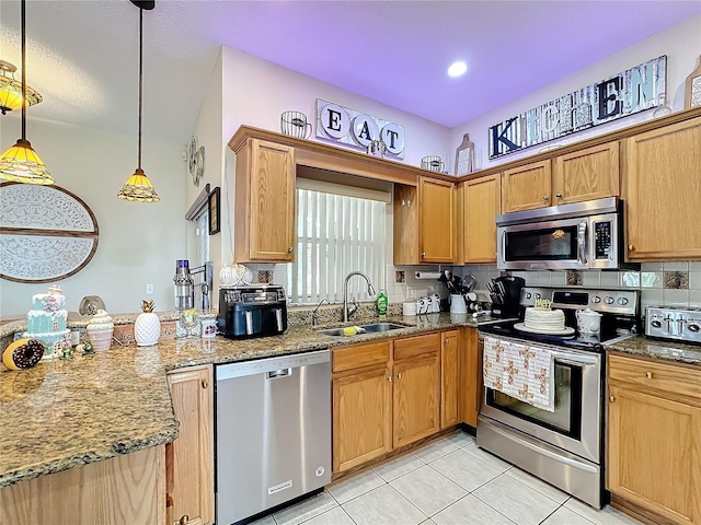 kitchen with pendant lighting, appliances with stainless steel finishes, sink, and dark stone countertops