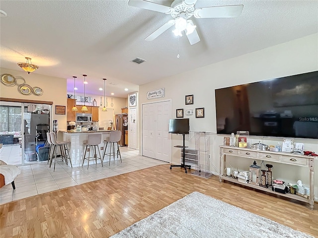 living room with a textured ceiling, ceiling fan, and light hardwood / wood-style flooring