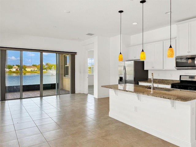 kitchen featuring sink, a water view, appliances with stainless steel finishes, a kitchen breakfast bar, and dark stone countertops