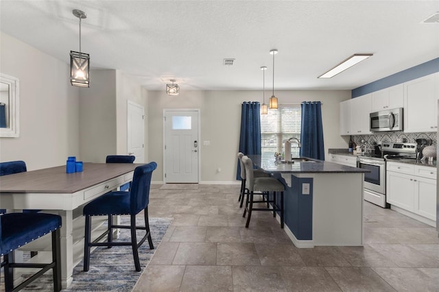 kitchen featuring appliances with stainless steel finishes, pendant lighting, a center island with sink, white cabinetry, and a breakfast bar area