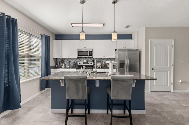 kitchen with a center island with sink, dark stone countertops, and appliances with stainless steel finishes