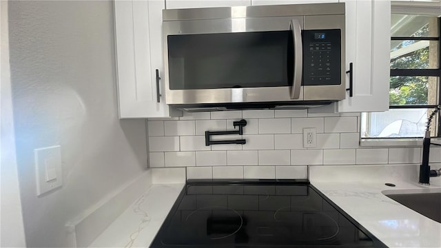 details featuring decorative backsplash, black electric stovetop, white cabinetry, and light stone counters