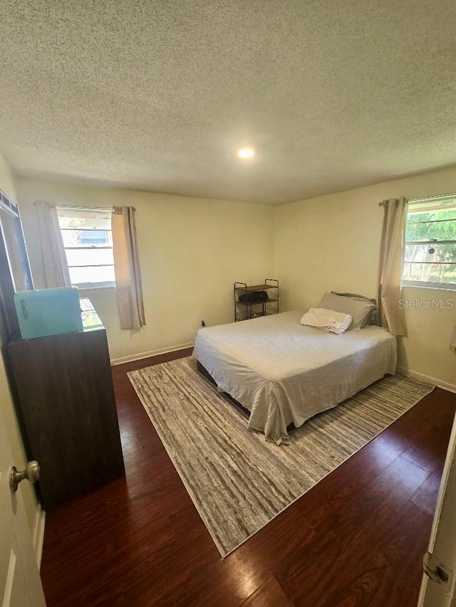 bedroom featuring a textured ceiling, multiple windows, and dark hardwood / wood-style floors