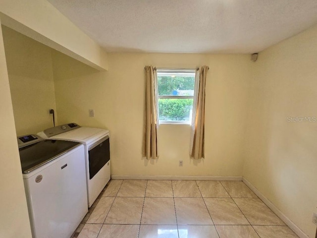 clothes washing area with a textured ceiling, separate washer and dryer, and light tile patterned floors