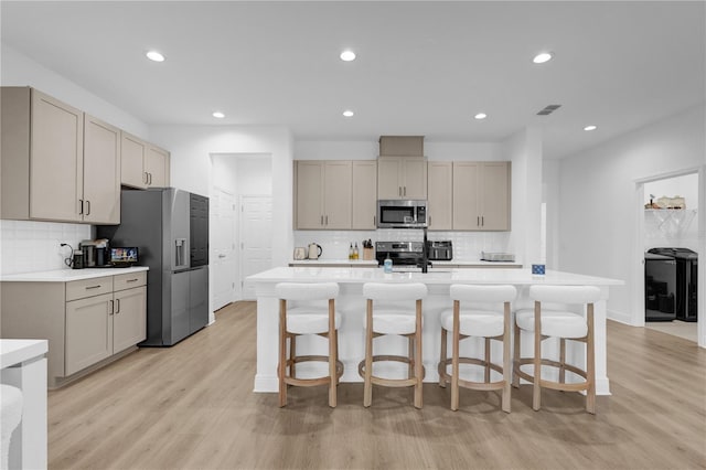 kitchen with a kitchen bar, stainless steel appliances, light hardwood / wood-style floors, an island with sink, and backsplash