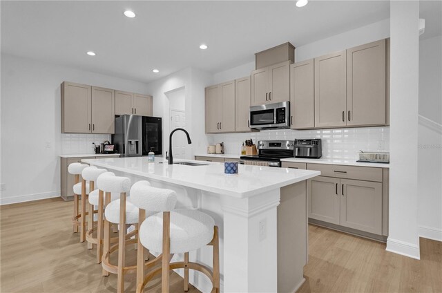 14442 Noto Ave, Clermont, FL 34714 - kitchen with stainless steel appliances, decorative backsplash, light wood-style floors, a kitchen island with sink, and a breakfast bar