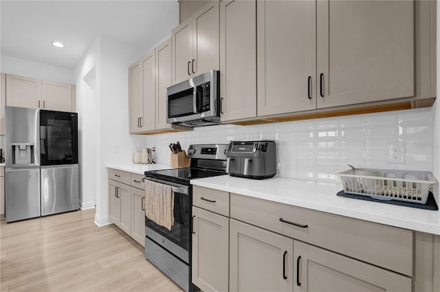 kitchen with gray cabinetry, light wood-type flooring, appliances with stainless steel finishes, and tasteful backsplash