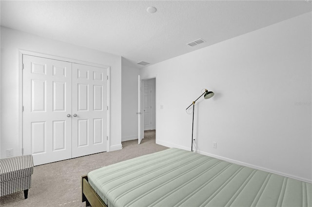 bedroom with a textured ceiling, light carpet, and a closet