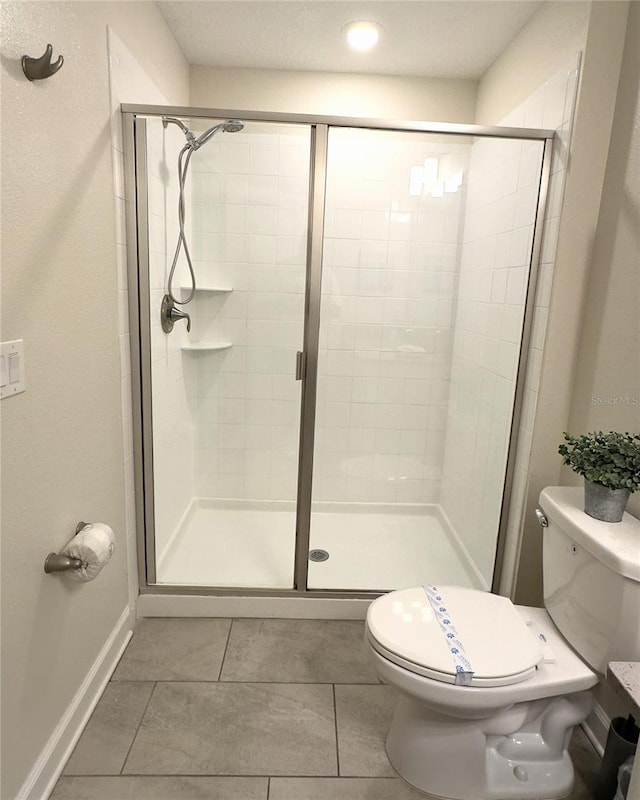 bathroom with tile patterned flooring, toilet, and a shower with door