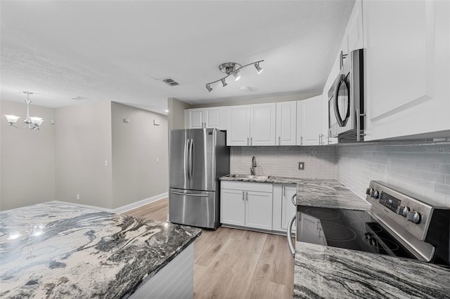 kitchen with white cabinets, stainless steel appliances, a chandelier, and dark stone countertops