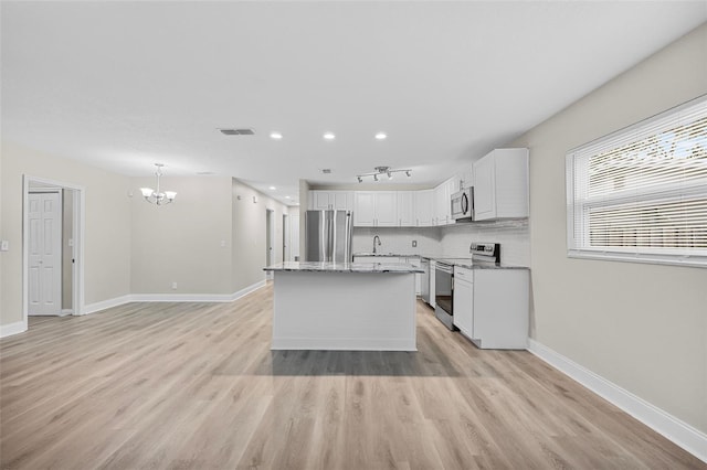 kitchen with stainless steel appliances, light hardwood / wood-style floors, white cabinetry, an inviting chandelier, and a kitchen island