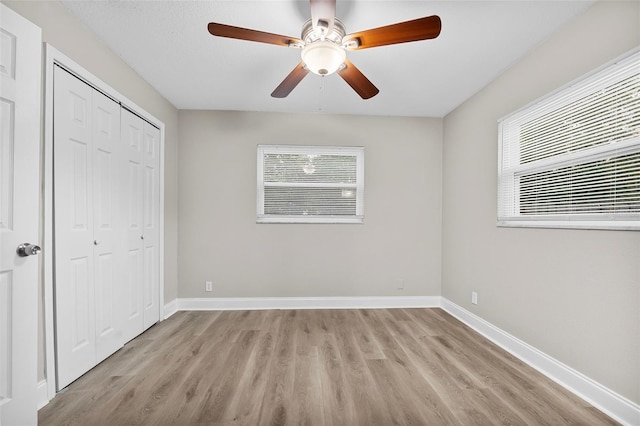 unfurnished bedroom with light hardwood / wood-style floors, multiple windows, ceiling fan, and a closet