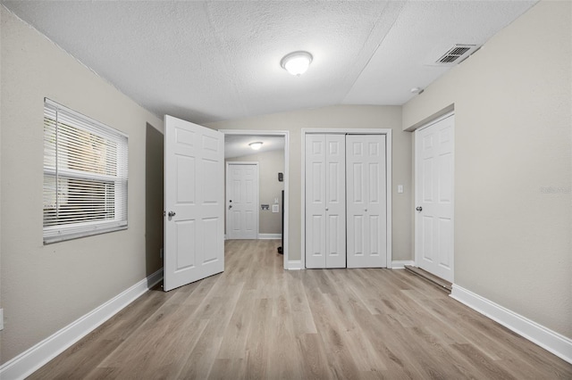 unfurnished bedroom with light wood-type flooring, a textured ceiling, and vaulted ceiling