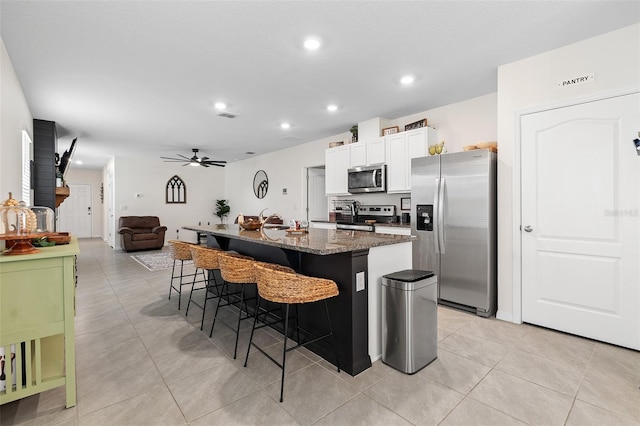 kitchen featuring stainless steel appliances, dark stone counters, a kitchen bar, a kitchen island with sink, and white cabinets