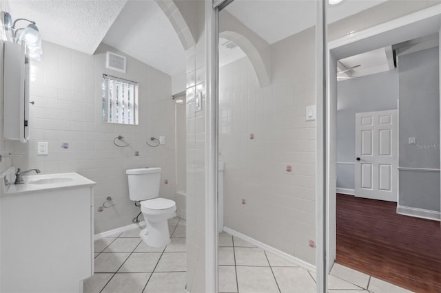 bathroom with tile walls, vanity, a textured ceiling, vaulted ceiling, and tile patterned flooring