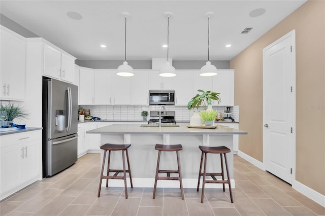 kitchen featuring stainless steel appliances, hanging light fixtures, a kitchen island with sink, white cabinets, and decorative backsplash