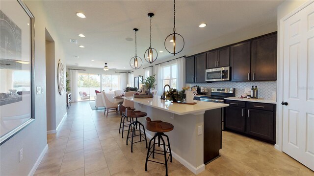 kitchen featuring stainless steel appliances, a kitchen bar, hanging light fixtures, an island with sink, and ceiling fan