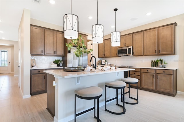 kitchen with stainless steel microwave, backsplash, a breakfast bar, an island with sink, and light countertops