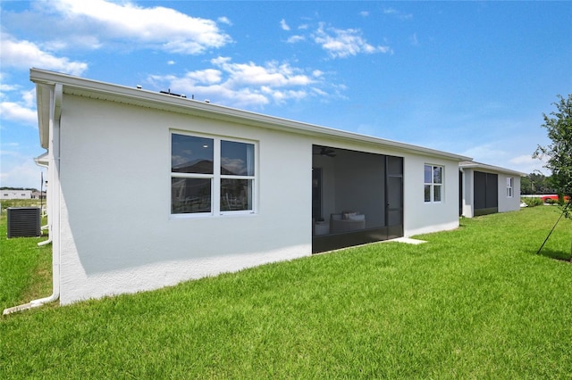 rear view of property with stucco siding, a lawn, central AC, and a sunroom