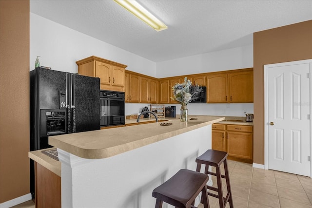 kitchen with black appliances, light tile patterned flooring, a kitchen bar, sink, and a kitchen island with sink