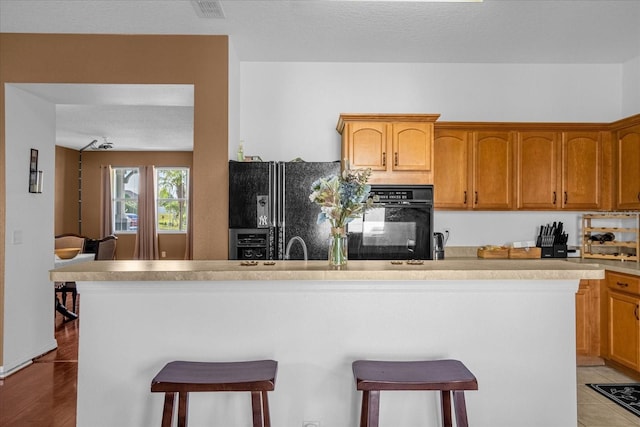 kitchen featuring black appliances, light hardwood / wood-style floors, a textured ceiling, and a kitchen breakfast bar