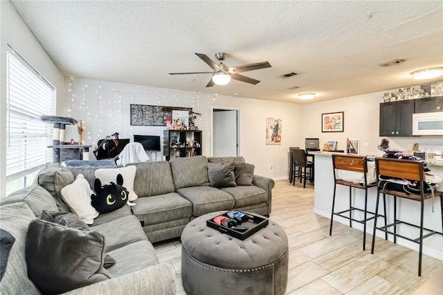 living room featuring ceiling fan, light hardwood / wood-style floors, and a textured ceiling