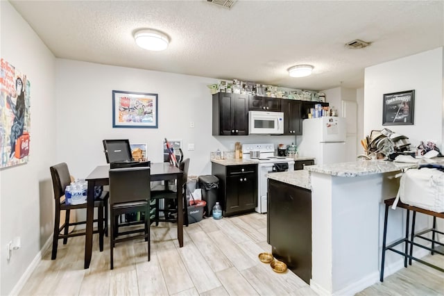 kitchen with light stone countertops, a kitchen breakfast bar, light wood-type flooring, white appliances, and a textured ceiling