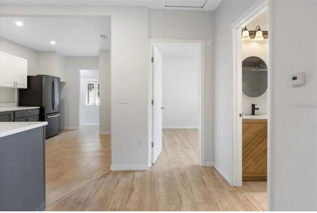 kitchen with light hardwood / wood-style floors, stainless steel refrigerator, white cabinetry, and sink