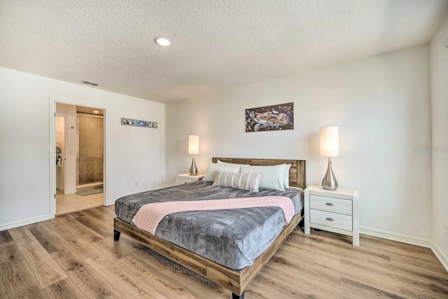 bedroom featuring ensuite bath, light hardwood / wood-style floors, and a textured ceiling