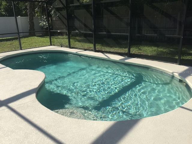 view of pool featuring a lawn and glass enclosure