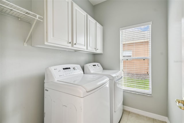 clothes washing area with washing machine and dryer, cabinets, and light tile patterned floors