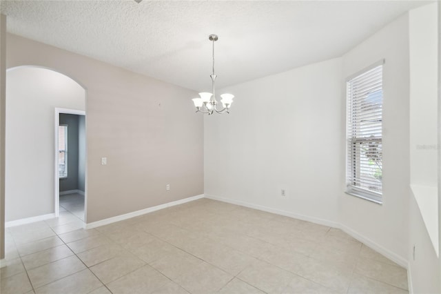 tiled empty room featuring a notable chandelier and a textured ceiling