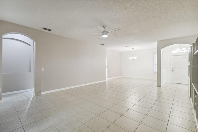 empty room with ceiling fan with notable chandelier, a textured ceiling, and light tile patterned floors