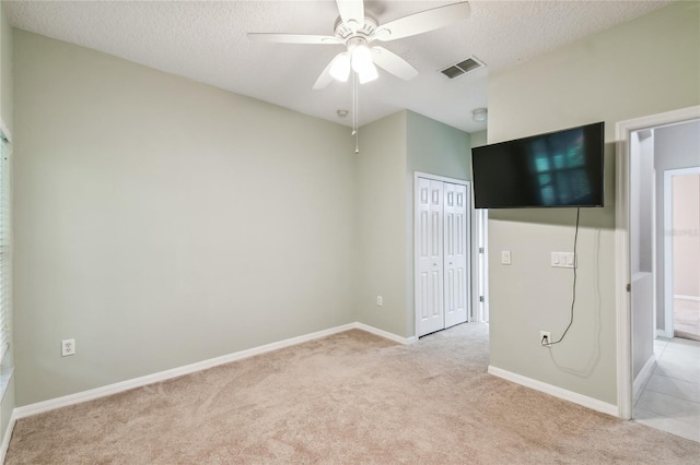 unfurnished bedroom featuring ceiling fan, a textured ceiling, a closet, and light colored carpet