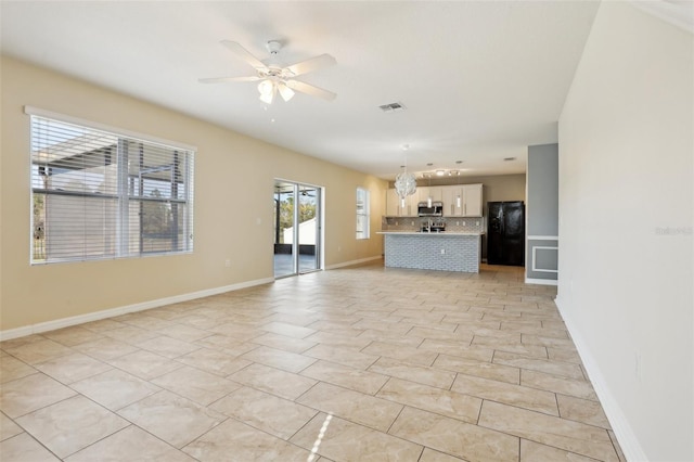 unfurnished living room with ceiling fan with notable chandelier, light tile patterned floors, and a healthy amount of sunlight