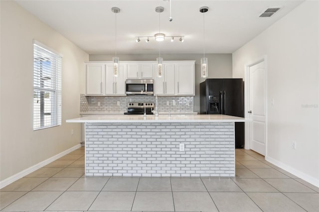 kitchen with decorative light fixtures, white cabinets, a kitchen island with sink, and appliances with stainless steel finishes