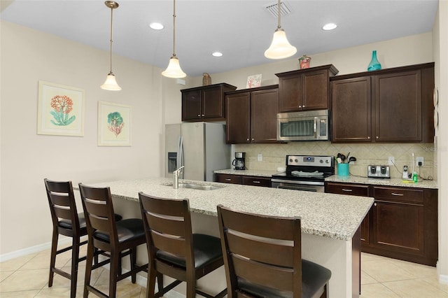 kitchen featuring stainless steel appliances, a breakfast bar area, a center island with sink, and pendant lighting