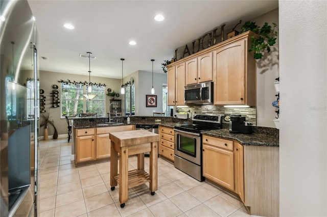 kitchen featuring stainless steel appliances, kitchen peninsula, sink, pendant lighting, and light brown cabinetry