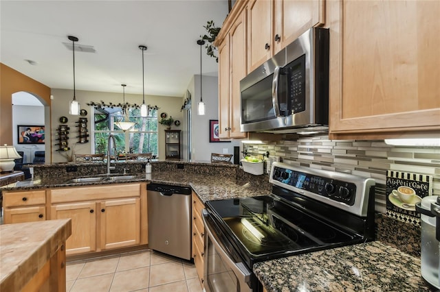 kitchen featuring sink, light tile patterned flooring, appliances with stainless steel finishes, decorative light fixtures, and dark stone countertops