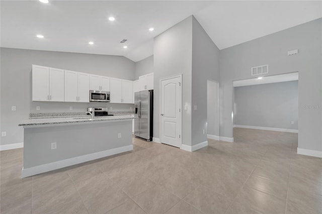 kitchen with light stone countertops, stainless steel appliances, white cabinets, and a center island with sink