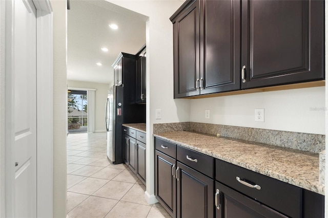 kitchen featuring dark brown cabinets, light stone counters, and light tile patterned floors