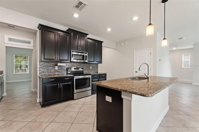 kitchen with a kitchen island with sink, appliances with stainless steel finishes, sink, and backsplash