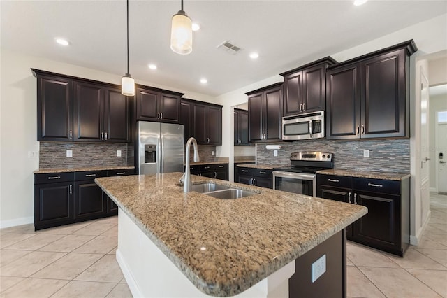 kitchen featuring decorative backsplash, hanging light fixtures, sink, a kitchen island with sink, and appliances with stainless steel finishes