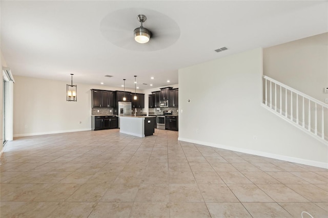 unfurnished living room featuring ceiling fan with notable chandelier, light tile patterned floors, and sink