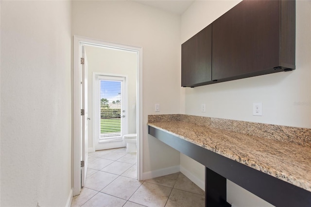 kitchen featuring dark brown cabinetry, light tile patterned floors, and light stone counters