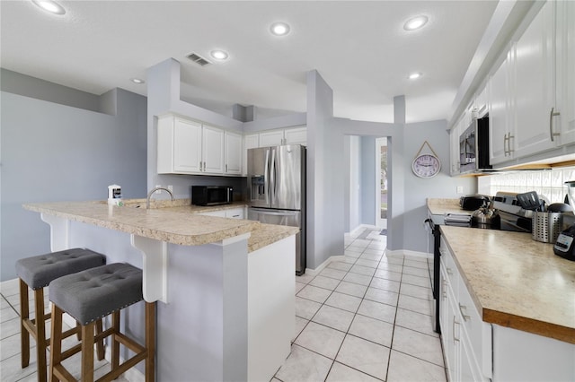 kitchen with kitchen peninsula, light tile patterned floors, a kitchen breakfast bar, white cabinetry, and appliances with stainless steel finishes