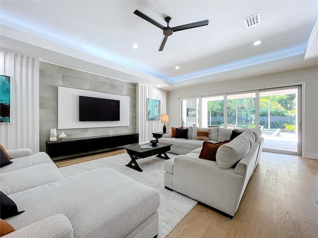 living room with a wealth of natural light, light hardwood / wood-style floors, and a tray ceiling