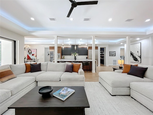 living room featuring ceiling fan with notable chandelier, a raised ceiling, and light wood-type flooring