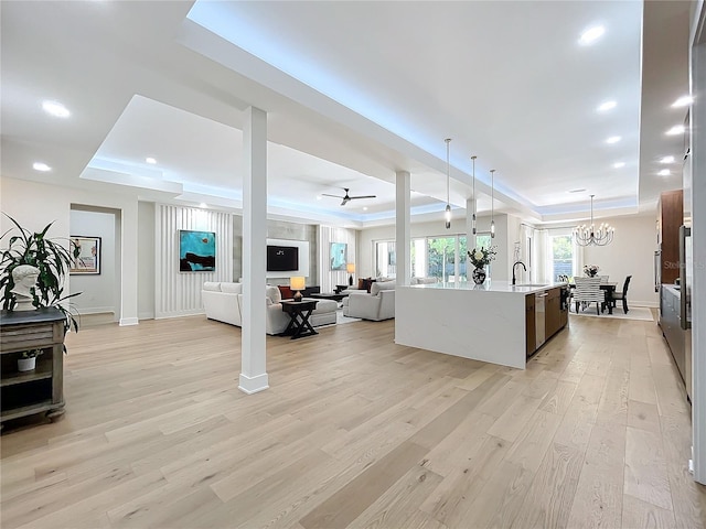 living room with ceiling fan with notable chandelier, light hardwood / wood-style flooring, sink, and a raised ceiling